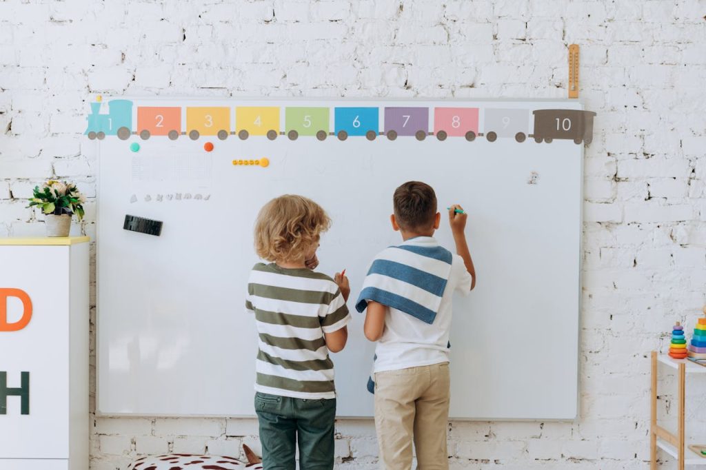 Two boys writing on a colorful classroom whiteboard, enhancing learning.