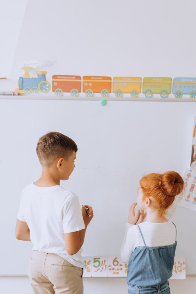 Two young children engaging in learning activities at a whiteboard in a preschool classroom.